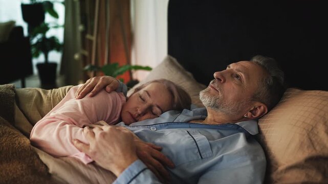 Pensive middle-aged man lying awake in bed and thinking beside his sleeping wife - Powered by Adobe