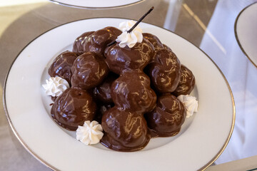 Plate of chocolate profiteroles filled with cream, a rich and indulgent Italian dessert. Close-up food photography perfect for pastry, gourmet sweets, and traditional Italian cuisine.