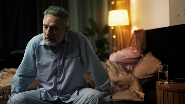Sad middle-aged man and wife sitting apart on bed, facing relationship issues