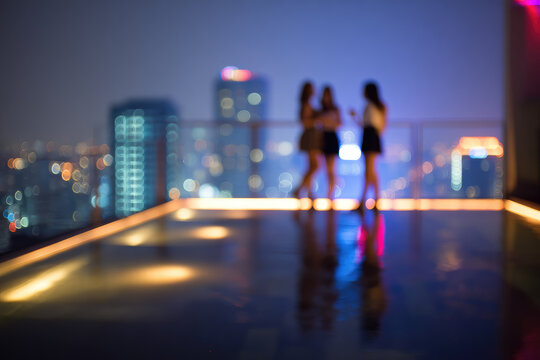 Defocused friends enjoying drinks on rooftop bar with blurred city lights, night urban skyline, social gathering, modern lifestyle, relaxed atmosphere, happiness - Powered by Adobe