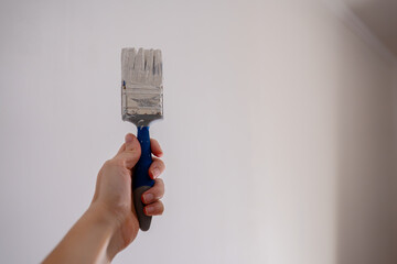 Close-up of a hand holding a paintbrush loaded with thick white paint, ready to apply the color to...