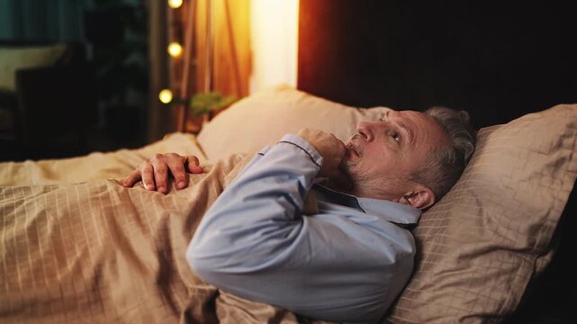 Sad man in his 50s lying in bed and trying to fall asleep, uncomfortable pillow