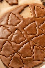 Rolled out pastry dough with cut out Christmas tree shapes on white marble table close up. Preparation of homemade gingerbread cookies