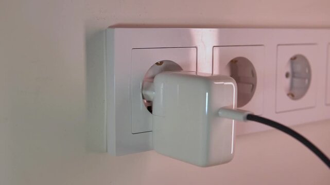 Hand plugging and unplugging white power adapter charger into wall electrical outlet home technology everyday routine device charging close-up energy supply