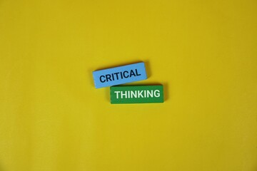 Two blocks labeled 'CRITICAL' and 'THINKING' rest on a yellow backdrop, symbolizing analysis, reasoning, and thoughtful decision making.