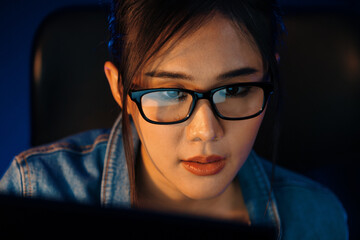 Portrait young beautiful Asian creative with glasses of serious face looking on pc to search project creator social media online, planning strategy creator at neon modern office at night. Stratagem.