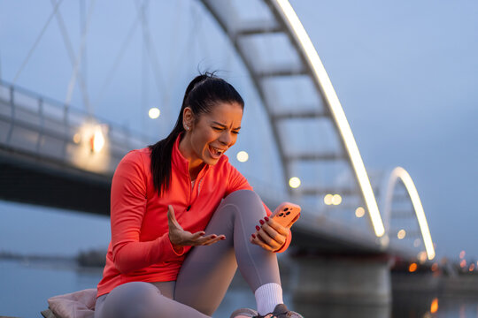 Woman reacting to bad news on her phone near a bridge at dusk