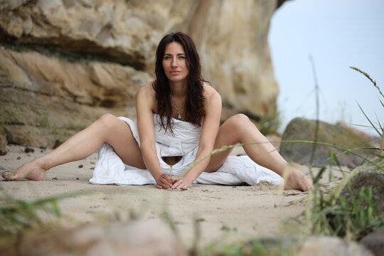 Woman relaxing on sandy beach wrapped in white blanket