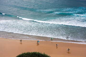 High-angle view of a crowd of surfers walking along the beach on the beautiful blue atlantic ocean