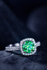 A green diamond ring with a white band sits on a black surface