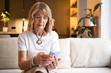 Senior woman relaxing on a couch, focused while browsing content on her smartphone