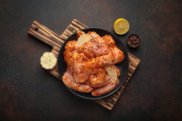 Raw marinated chicken wings spices garlic lemon black plate wooden cutting board cooking