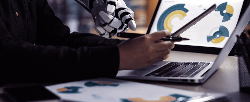 A sleek robotic arm collaborates with a human in a modern workspace, displaying digital graphs and analytics on a laptop, symbolizing innovation and technology integration.Noogenesis - Powered by Adobe