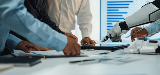 A modern business meeting showcasing collaboration between human hands and a robotic arm over a digital tablet in a sleek office environment.Noogenesis