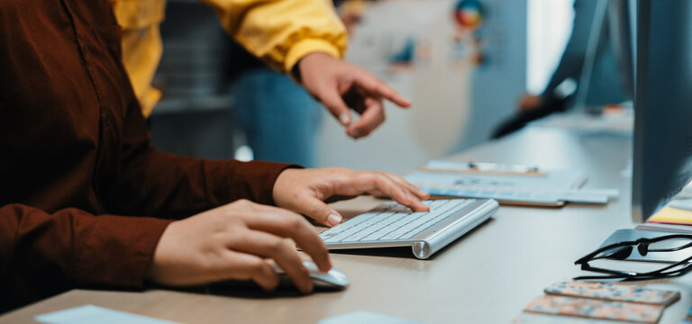 A dynamic scene of a creative workspace displaying a closeup of hands on a keyboard, highlighting collaboration and interaction among team members engaged in discussions. SACTR