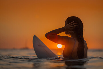 Surfer girl sitting on surfboard at sunset
