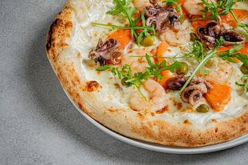 A tantalizing seafood pizza showcases shrimp and octopus with vibrant vegetables on a gray surface