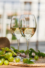 Closeup of white wine glasses with green grapes on wicker placemat and outdoor background