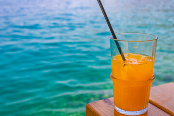 Glass of orange juice with a straw against sea background