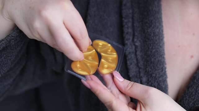 Adorable curly woman glancing straight on camera. Happy woman smiling and using gold eye patches with collagen, peptide, ceramide and hyaluronic acid, derma oil. Dermatology, healthy skin concept.