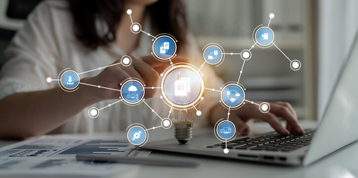 A focused businesswoman interacts with a laptop, showcasing a light bulb symbolizing innovation and digital icons representing technology and creativity in her workspace. Crux