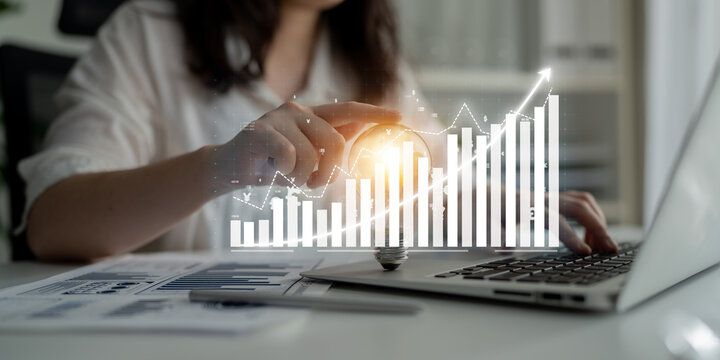 A business professional analyzes financial data using a laptop, visualizing growth trends with digital graphs in a modern office environment. Impute
