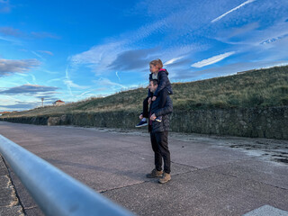 Father Holding Daughter on Shoulders at Seaside Walk