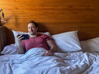 Man Watching Smartphone While Relaxing in Bed in Wooden Cabin
