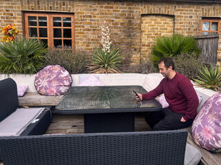 Man Relaxing Outdoors on Patio Sofa Using Smartphone