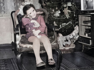 Vintage portrait of a little girl with bows sitting in a chair and hugging a doll. Retro photo from 1973.