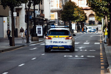 Police vehicle driving down a city street with clear road markings and trees lining the sidewalk, showcasing urban life and law enforcement presence in a bustling environment © wedmoments.stock