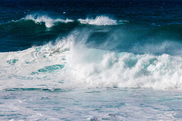 Powerful ocean waves crashing against the shore, creating a dynamic scene of frothy white water and deep blue sea, capturing the essence of nature's raw beauty and energy