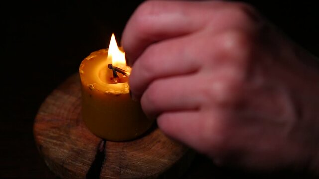 Woman hand lights a match the bees wax candle on wooden candlestick for mood, relaxation, meditation dark black background. Person lighting the decoration handmade single candle flame