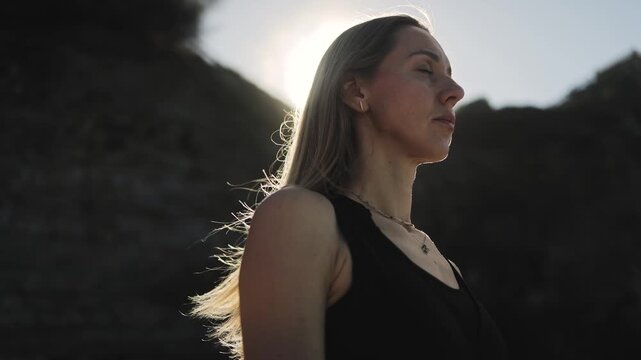 Close-up portrait of a healthy woman meditating with closed eyes on a dark background with sun rays, mental health, meditation, yoga, tantra, mantra, spirituality, sports, breathing, hope, healing