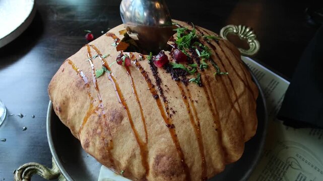 fancy elaborate fattoush salad inside a fried crispy pita bread shell being broken before eating with a spoon (middle eastern lebanese israeli syrian appetizer with pomegranate molasses and seeds)