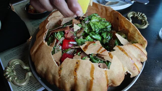 fancy elaborate fattoush salad inside a fried crispy pita bread shell being broken before eating with a spoon (middle eastern lebanese israeli syrian appetizer with pomegranate molasses and seeds)