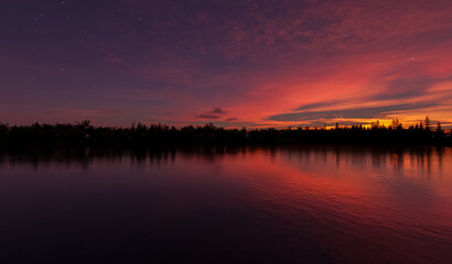 Sunset Over Calm Lake With Silhouetted Trees, Starry Sky, And Reflections