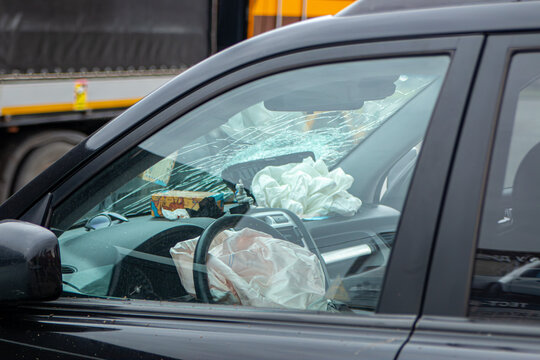Deployed airbags inside a damaged car after a road traffic accident, seen through a broken windshield. Interior of vehicle showing safety system activation after collision.
