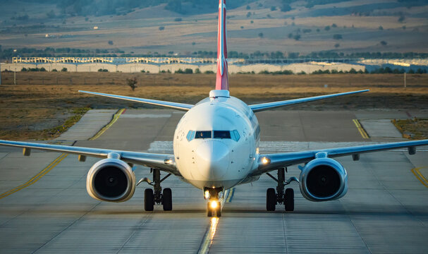 Symmetrical front shot of an airplane on the ground at the airport with visible turbine blades and cockpit windshield reflecting the daylight environment