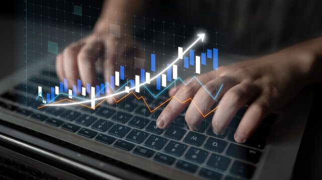 A close-up shot of hands typing on a laptop keyboard with an overlay of financial data visualization, including graphs and charts illustrating market growth and trends. Impute