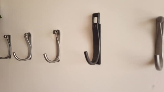 Four Assorted Metal Coat Hooks Mounted On A Beige Wall With Green Vine Garland