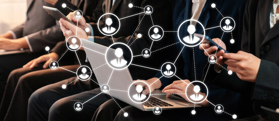 Individuals engage in a professional networking event, utilizing smartphones and laptops to foster connections, ideas, and collaboration in a corporate atmosphere. Amity