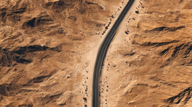 Aerial View of Curved Road Through Arid Desert Landscape with Rugged Terrain and Dry Earth Tones