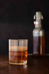 A vintage rocks glass partially filled with brown alcohol, bottle in background 