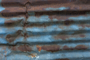 Corrugated weathered zinc metal sheet displaying blue patina and prominent dark brown rust stains