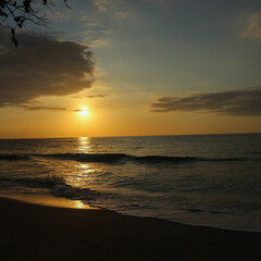 Golden hour beach sunset. Ocean waves reflect the dramatic sky and sun's brilliant light. Serene nature background