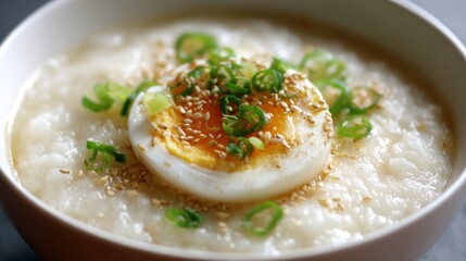 Creamy Rice Congee with Soft Boiled Egg and Green Onions, Garnished with Sesame Seeds in a White Bowl