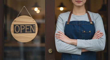 A female cafe owner stands with arms crossed at the open door of her business. An 'OPEN' sign hangs on the glass