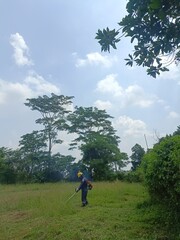 workers whose job is to cut grass in the open field area for oil and gas extraction, working under the bright blue sky and green nature, 