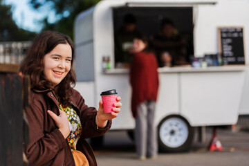 young woman in her late teens holding warm drink in disposable cup by local business coffee van